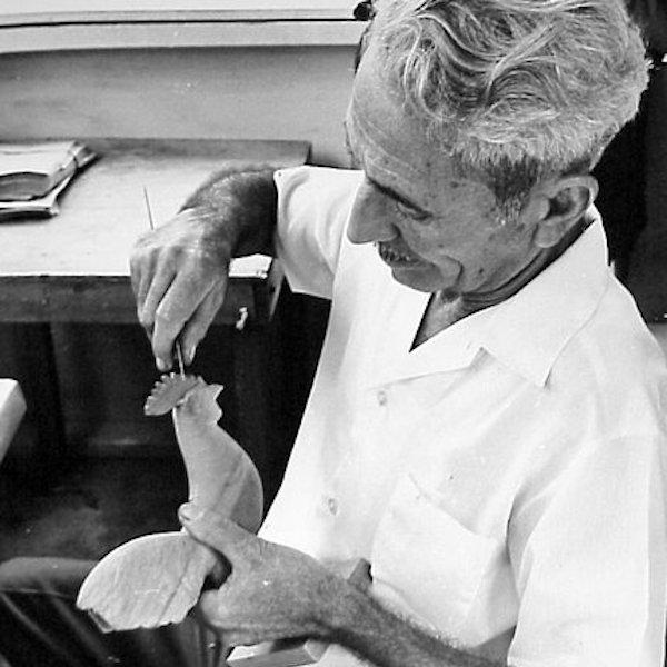 A man carving a wooden rooseter figurine.
