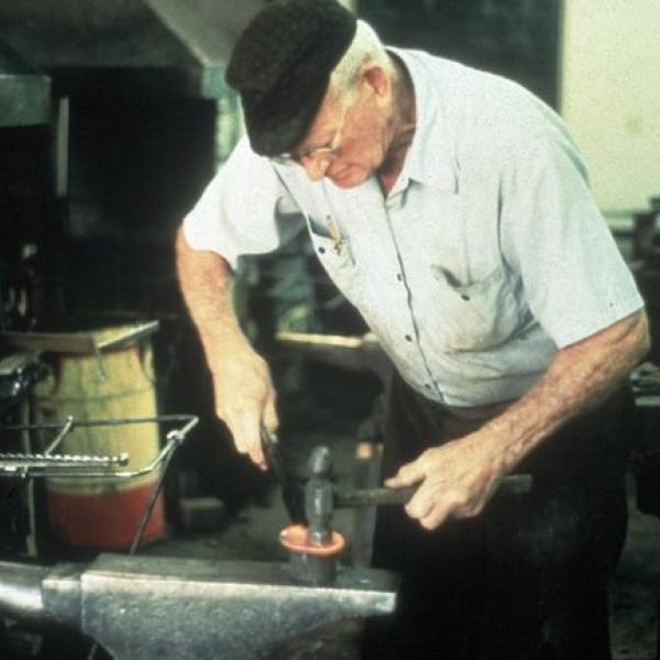 A man stooping over an anvil.