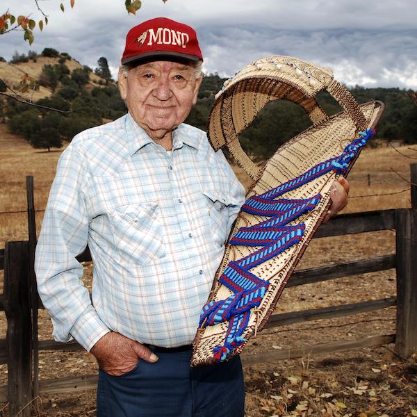 A man holding a traditional baby crib. 