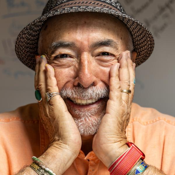 A man in a straw hat, with a broad smile, holding his head in his hands