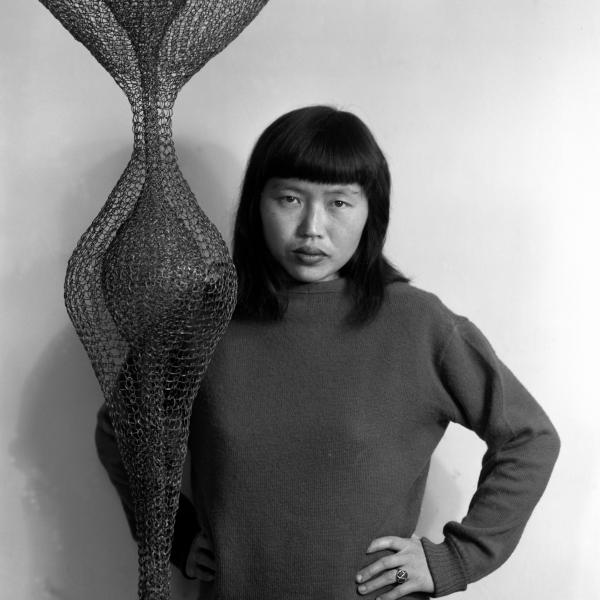 Woman with medium black hair wearing a sweatshirt in front of hanging wire artwork. 