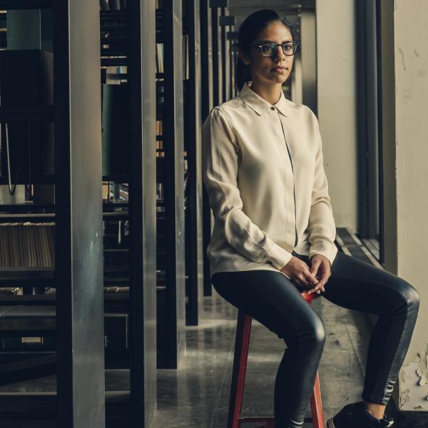 Woman wearing glasses and a beige sweater sitting on a chair. 