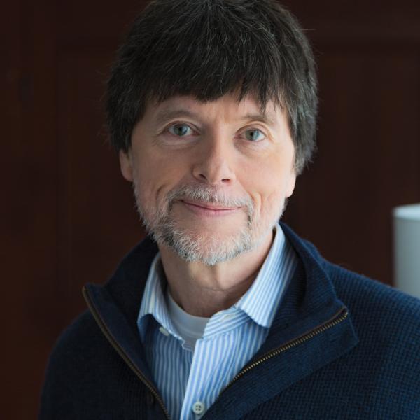 Man with short dark hair and gray beard wearing a sweater and dress shirt posing for portrait.