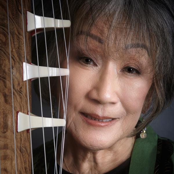 Photo of an Asian woman smiling next to a koto instrument