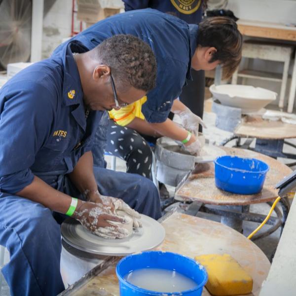 Seated man looks down at clay on a round surface while he works it with his hands