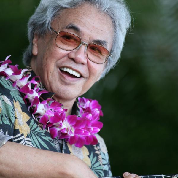 Man with gray hair and glasses playing a ukelele.