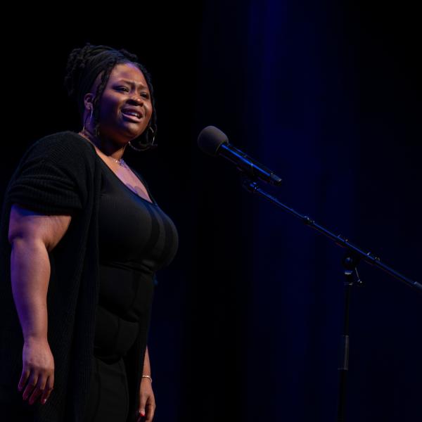 A young woman in a black dress speaks at a microphone