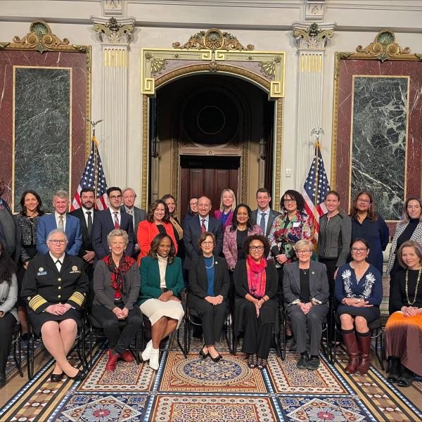 A large group of people pose for a photo in front of two American flags.