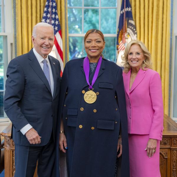 Black woman in blue jacket wearing a medal around her neck surrounded by older man wearing a blue suit and woman with blonde hair wearing a pink suit. 