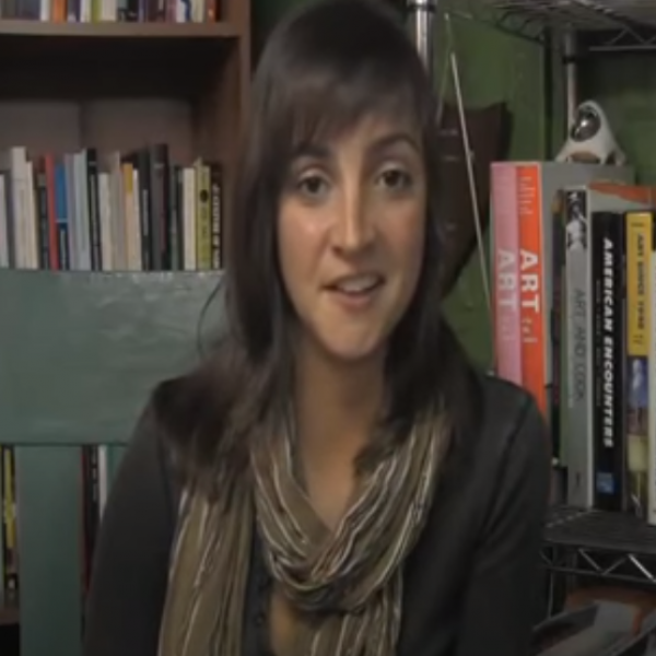 Woman talking in front of bookshelves.