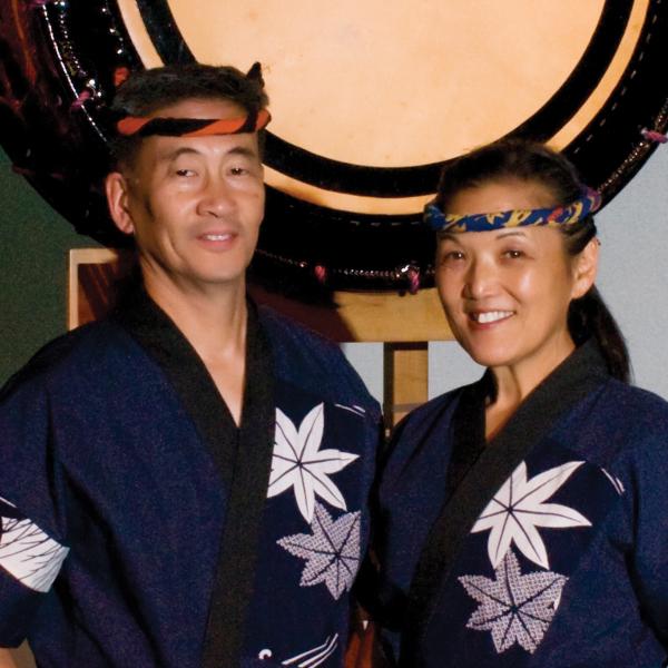 Asian man and woman standing in front of large drum. 