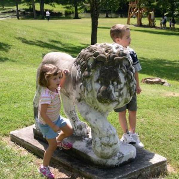 two young children play around a stone lion outdoors