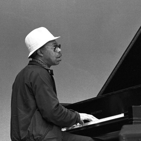 Man in white hat playing piano on stage. 