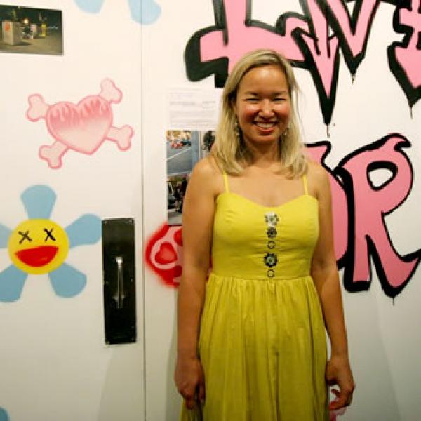 Philippa Highes in a yellow dress in front of a humorous wall art piece