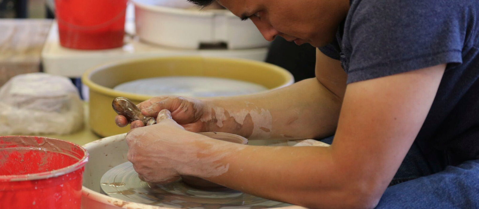 Seated man bent over working a pottery wheel