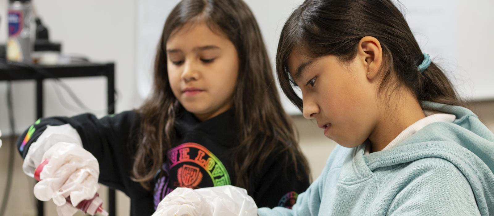 Two girls gluing items during an arts class.