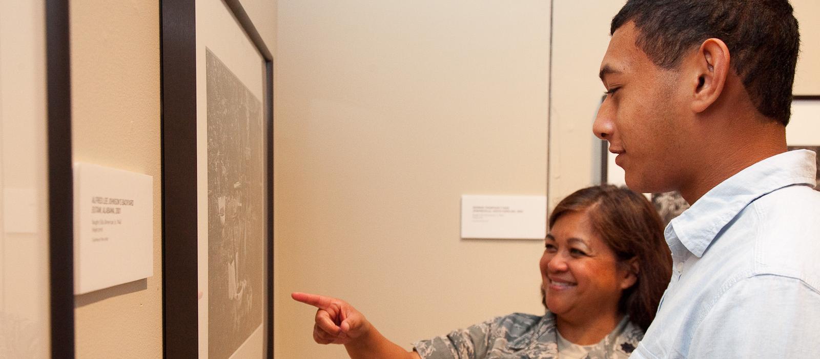 Woman in uniform and her son look at artwork in museum.