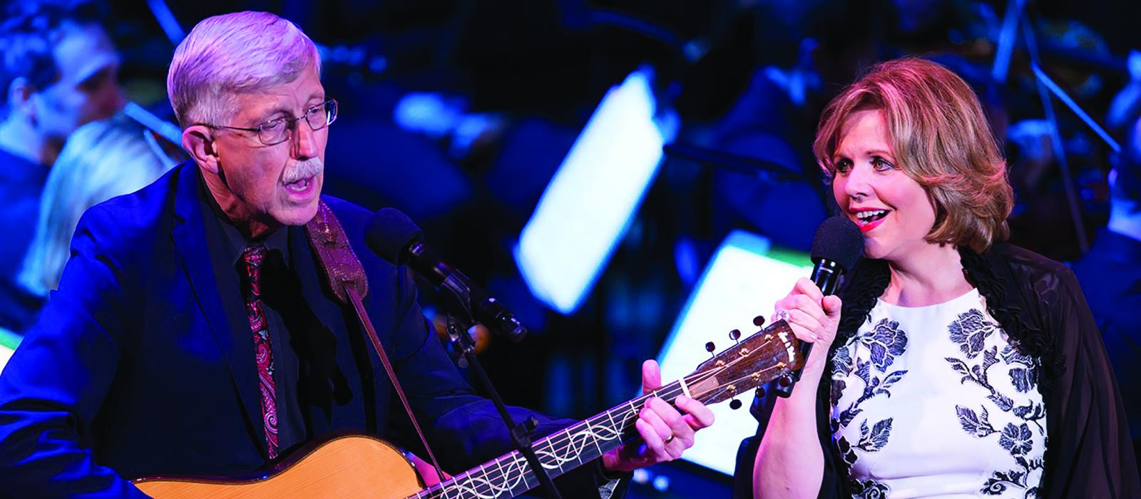 Older man playing guitar next to woman singing. 