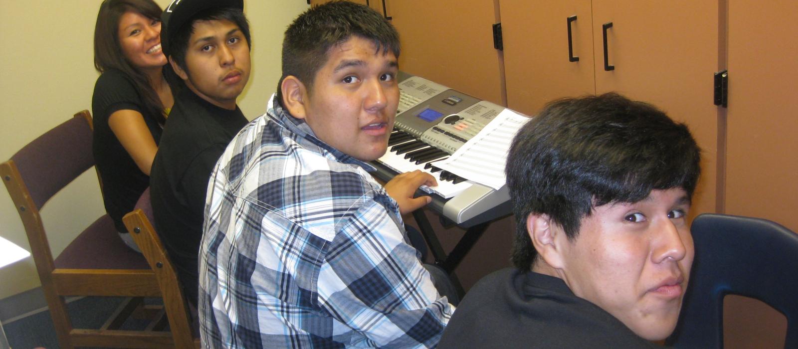 Three male and one female Native students sitting in front of a keyboard and turned to face the camera.