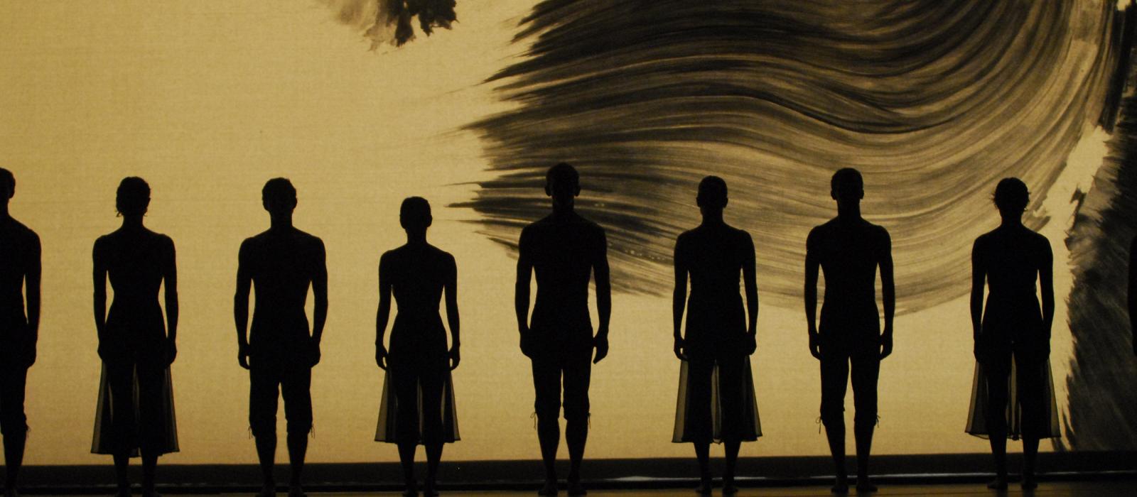 Shadows of dancers in front of a painting on stage.