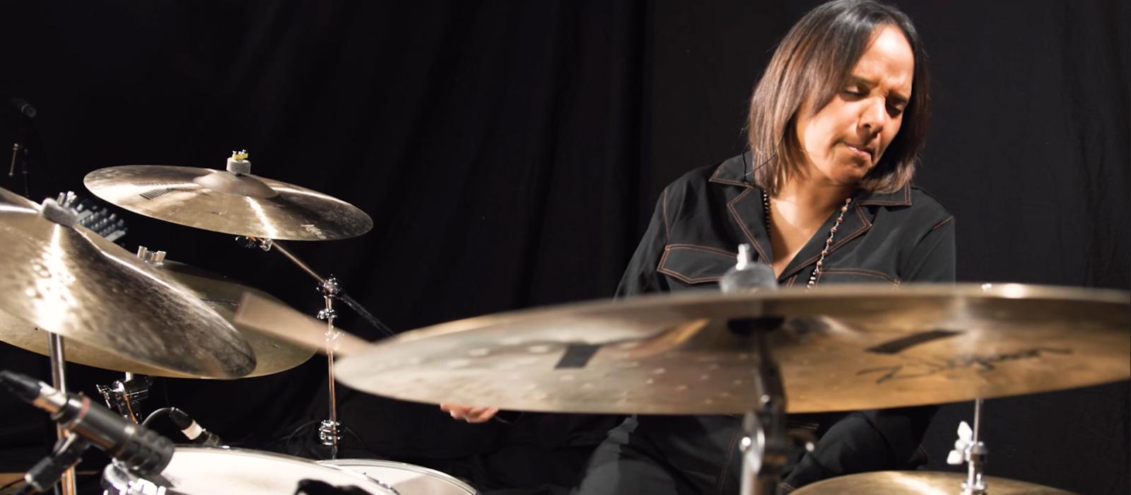 Woman with long brown hair playing drums. 