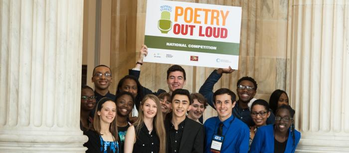 A group of student stand together holding up a Poetry Out Loud poster.