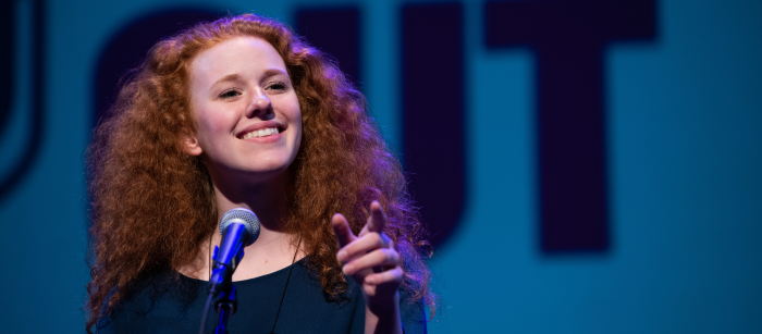 A young woman wearing a green blouse speaks into a microphone.