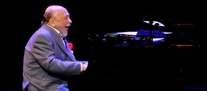 Man playing piano on stage, laughing.