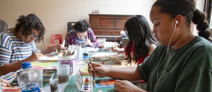 Group of kids sitting at table painting.