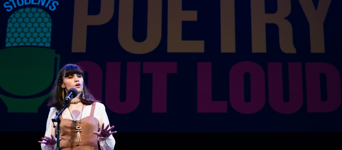 A young woman speaks into a microphone on a darkened stage. The Poetry Out Loud logo is projected behind her.