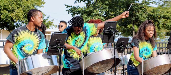 Three people in tie-dye shirts play steel drums at an outdoor venue