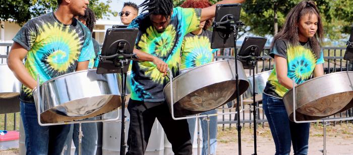 Three people in tie-dye shirts play steel drums at an outdoor venue