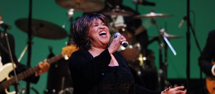 Black woman in black dress singing on stage. 