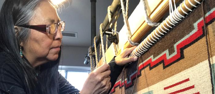 Native woman with glasses weaving on a loom.