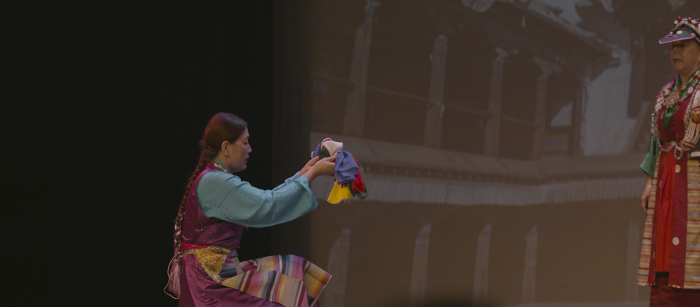 Asian woman in purple dress holding a cloth on stage.