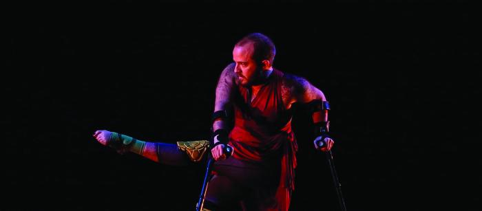 Man with short hair and beard on crutches dancing on stage. 