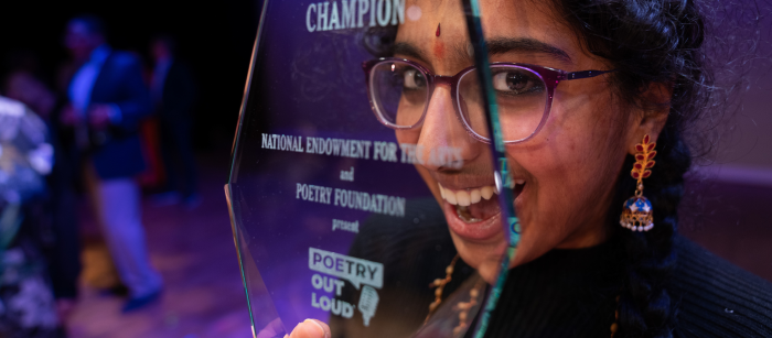 A young woman poses with a wide smile, looking through her award declaring her as the National Champion.
