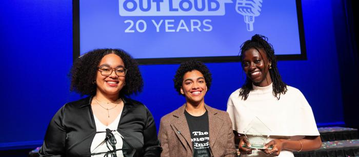 Three smiling students smile hold trophies in front of a Poetry Out Loud backdrop.