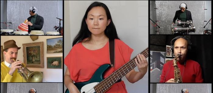 Screen shot with women in red playing bass in middle, trumpeter in hat in middle box to left and saxophonist in box to right and a percussionist in all the corner boxes. 
