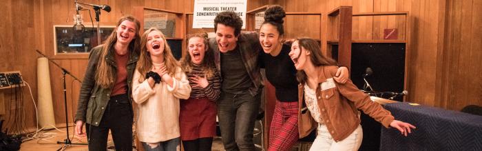 Group of teens in recording studio laughing.
