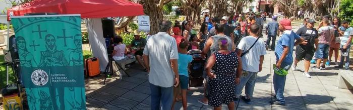 Long line of people along a sunny outdoor walkway participating in a hurricane relief event with artists