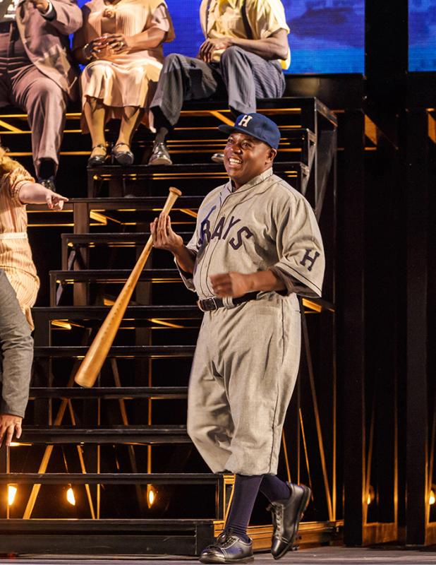 Man in baseball uniform holding a bat on stage. 