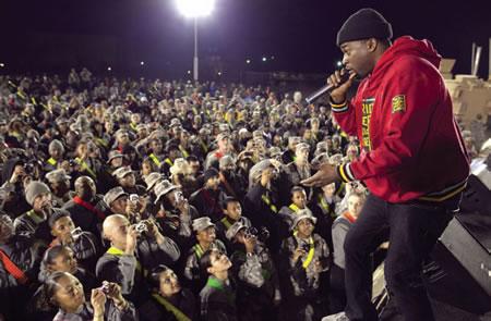 David Banner USO African-American man in red sweat jacket and wearing black hat rapping to a crowd of servicemen.