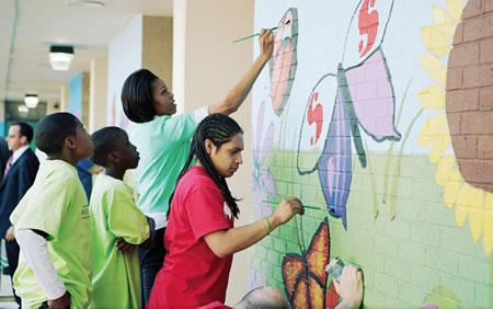 Michelle Obama and young African American students painting a mural on a brick wall