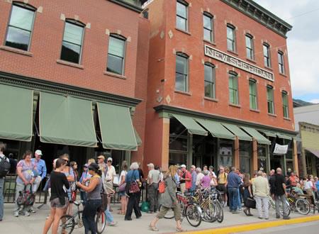 People standing in a line in front of old brick buildings with green awnings to get tickets to a movie.
