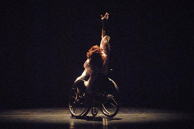 Mary Verdi-Fletcher A dancer in a wheelchair lifts one hand upward as she performs onstage
