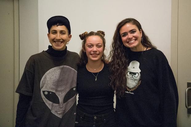 Three people stand posing for a photo in a recording studio, arms around each other, smiling.