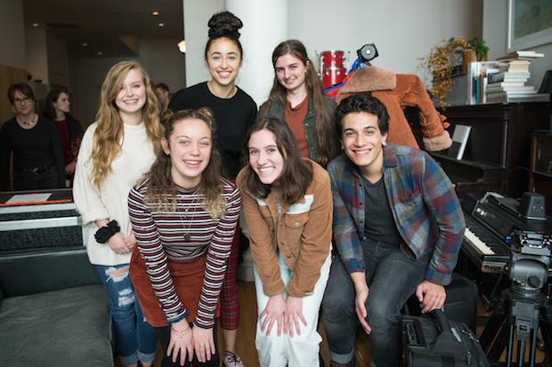 Five young women and a young man pose for a photo in a recording studio, smiling.