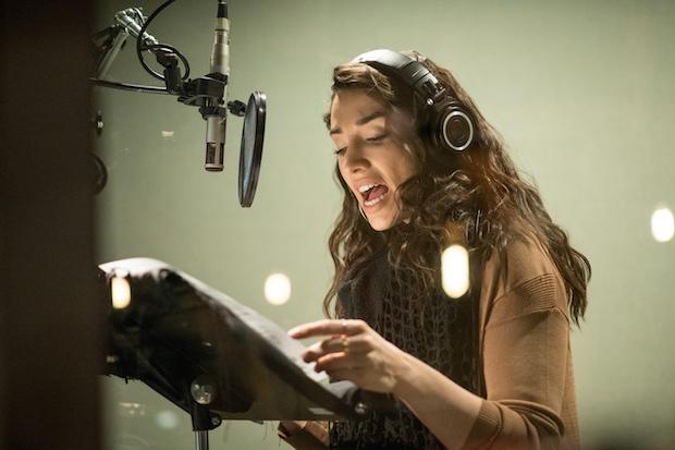 A woman wearing headphones sings into a suspended mic in a recording studio.