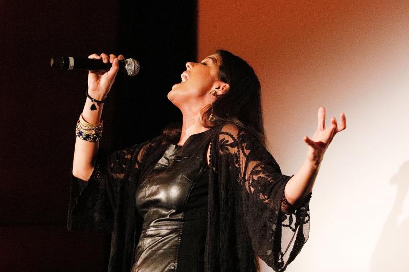 Arianna Asfar A woman sings into a microphone while throwing her head back